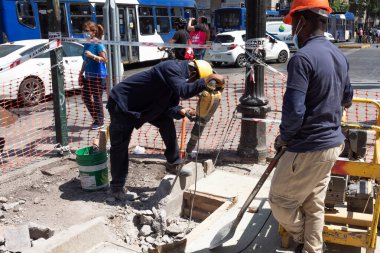 Santiago de Chile, Şili, 27-06-2021: Biri sarı kask takan iki adam kaldırımda çalışıyor. Diğer adam bir kaya matkabı tutuyor..
