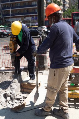 Santiago de Chile, Şili, 27-06-2021: İki adam bir inşaat alanında çalışıyor, biri sarı kask takıyor. Diğer adam turuncu bir kask takıyor..