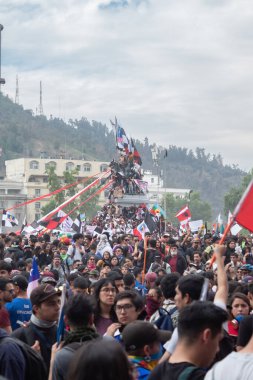 Santiago de Chile - Şili, 25-10-2019: Büyük bir kalabalık, bazıları kırmızı, beyaz ve mavi olmak üzere bayraklar ve pankartlar kaldırıyor. Etkinliğe her yaştan insanın katıldığı atmosfer canlı ve enerjik.
