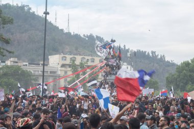 Santiago de Chile - Şili, 25-10-2019: Üzerinde siyah haç olan beyaz ve kırmızı bir bayrak da dahil olmak üzere büyük bir insan topluluğu çeşitli bayrakları elinde tutuyor
