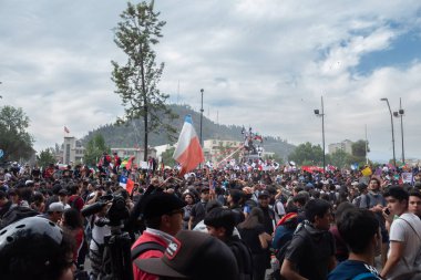 Santiago de Chile - Şili, 25-10-2019: Bir şehir meydanında büyük bir kalabalık toplandı, ellerinde bir bayrak var. Atmosfer canlı ve enerjik. Her yaştan ve geçmişden insanlar kutlama ya da protesto için bir araya geliyor.