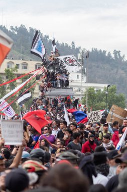 Santiago de Chile - Şili, 25-10-2019: Bir şehir meydanında büyük bir kalabalık toplandı, elinde işaretler ve bayraklar var. Sahne, insanların fikirlerini ve desteklerini dile getirmek için bir araya geldiği protesto ve birliktir.