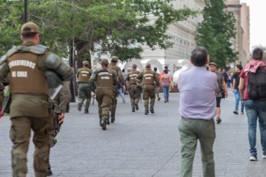 Santiago de Chile - Şili, 25-10-2019: Askeri üniformalı bir grup adam sokakta yürüyor. Adamlar yeşil ve kahverengi üniformalar giyiyorlar ve sırt çantaları taşıyorlar. Sahne ciddi ve odaklı.