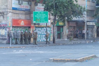 Santiago de Chile, Şili, 25-10-2019: Bir grup asker, üzerinde grafiti olan bir binanın önündeki sokak köşesinde duruyor. Askerler kask takıyor ve kalkanları var.