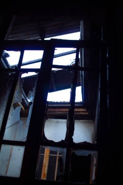 Kırık camlı ve üzerinde çatı olan bir pencere. Sahne karanlık ve kasvetli.