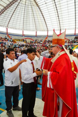 Tumbes, Tumbes, Peru 21-10-2023, Doğrulama Ayini: bir rahip genç bir adama kravat veriyor. Rahip kırmızı bir bornoz giyiyor ve genç adam beyaz bir gömlek giyiyor.