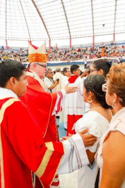 Tumbes, Tumbes, Peru 21-10-2023, Onaylama Ayini: Bir rahip bir grup insanı kutsuyor. Rahip kırmızı bir bornoz ve kırmızı bir şapka giyiyor. İnsanlar onun etrafında toplanıyor, bazıları ona sarılıyor. Atmosfer sıcak.