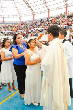 Tumbes, Tumbes, Peru 21-10-2023, Onaylama Ayini: Bir rahip beyaz elbiseli genç bir kadını kutsar. Rahip beyaz bir bornoz ve altın bir haç giyiyor. Rahip, kalabalığın önünde kadını kutsuyor.
