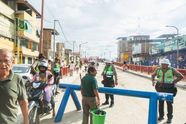 Tumbes, Tumbes, Peru 01-03-2025: Önlerinde mavi bir bariyer bulunan bir grup insan sokakta duruyor. Motosikletli birkaç polis memuru ve birkaç kişi var. Sahne gergin ve ciddi.