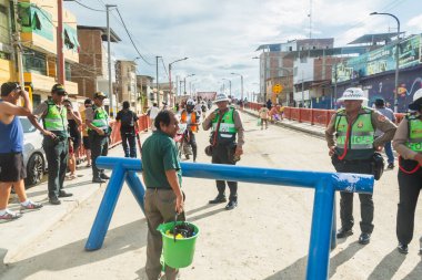 Tumbes, Tumbes, Peru 01-03-2025: Bir grup polis memuru mavi bariyerin önünde duruyor. Yeşil gömlekli bir adam kova tutuyor.