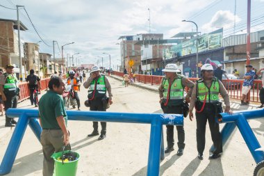 Tumbes, Tumbes, Peru 01-03-2025: Bir grup polis memuru, arkasında bir kalabalık ile mavi bariyerin önünde duruyor. Memurlar yansıtıcı yelek giyiyorlar ve trafiği yönlendiriyor gibi görünüyorlar. Sahne gergin.