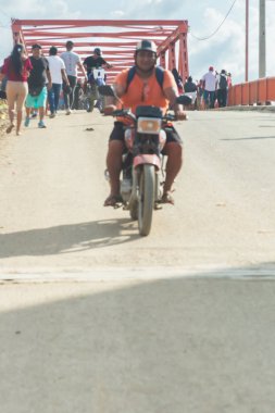 Tumbes, Tumbes, Peru 01-03-2025: Motosikletli bir adam arkasında bir kalabalık ile yolda ilerliyor. Sahne hareketli ve hareketli, insanlar yürüyor ve konuşuyor. Motosiklet sürücüsü ilgi odağı gibi görünüyor.