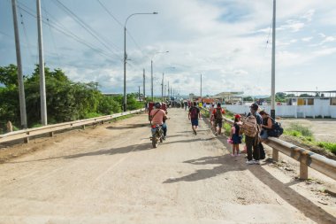 Tumbes, Tumbes, Peru 01-03-2025: Bir grup insan motosiklet ve sırt çantalarıyla toprak yolda yürüyor. Sahne bir seyahat ve maceradır.