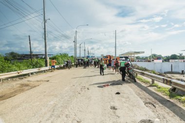 Tumbes, Tumbes, Peru 01-03-2025: Bir grup insan toprak yolda yürüyor. Yol elektrik kablolarıyla kaplı ve arka planda birkaç kamyon var. Sahne biraz kaotik ve düzensiz.
