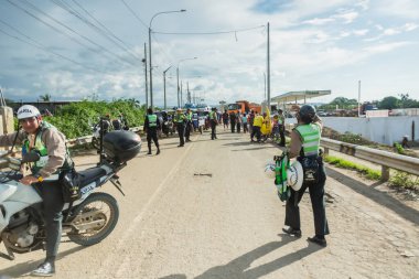 Tumbes, Tumbes, Peru 01-03-2025: Ön planda motosikletli bir grup insan bir yolda duruyor. İnsanlar güvenlik kıyafeti giyip sıraya girmiş gibi görünüyorlar.