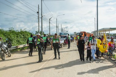 Tumbes, Tumbes, Peru 01-03-2025: Bir grup insan sokakta ortada bir polis memuruyla yürüyor. Polis memuru yeşil bir yelek ve siyah bir şapka giyiyor.