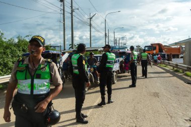 Tumbes, Tumbes, Peru 01-03-2025: Bir grup polis memuru, birinin yeşil yelek giydiği bir yolda duruyor. Polisler kuyrukta bekliyorlar ve arka planda bir kamyon ve bir otobüs de dahil olmak üzere birkaç araç var.