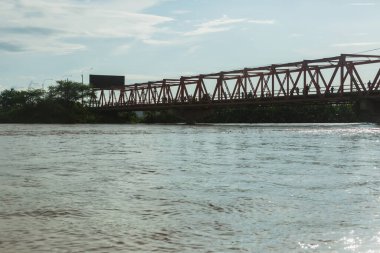 Bir köprü, arkasında reklam panosu olan bir nehri kapsar. Köprü kırmızıdır ve nehrin tüm genişliğini kaplar.