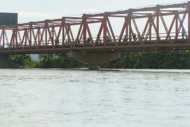 Nehrin üzerinde insanların yürüdüğü bir köprü. Köprü kırmızı ve su sakin.