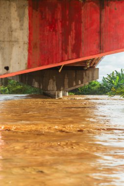 Kırmızı ve beyaz şeritli bir köprü gösterilir. Su kahverengi ve köprü kısmen sular altında.