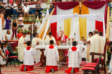 Tumbes, Tumbes, Peru 21-10-2023, Onaylama Ayini: Bir grup rahip beyaz cüppeli bir adamın elinde bardak ile masanın önünde diz çöküyor. Sahne dini bir tören ya da toplantı gibi görünüyor.