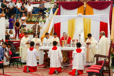 Tumbes, Tumbes, Peru 21-10-2023, Doğrulama Ayini: Bir grup rahip üzerinde beyaz bir bez olan bir masanın önünde diz çöküyor. Kırmızı bornozlar giyiyorlar ve etrafları insanlarla çevrili. Sahne kutsal ve dindardır.