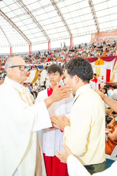 Tumbes, Tumbes, Peru 21-10-2023, Onaylama Ayini: Bir rahip sarı gömlekli genç bir adamı kutsuyor. Rahip beyaz bir bornoz ve kırmızı bir eşarp giyiyor. Arka planda bir sürü insan var.