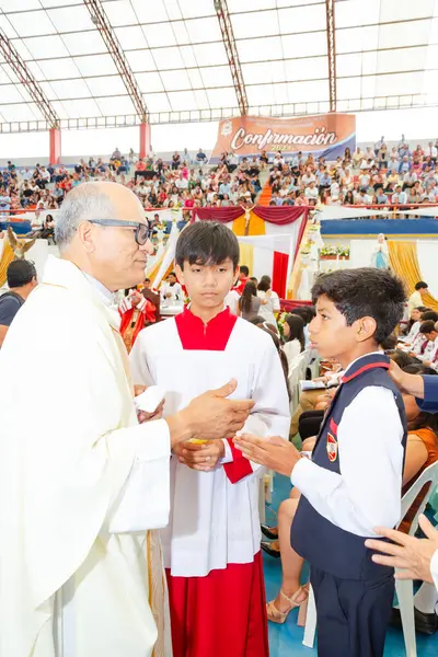 Tumbes, Tumbes, Peru 21-10-2023, Onaylama Ayini: bir rahip iki genç çocuğu kutsuyor. Rahip beyaz bir bornoz giyiyor ve çocuklar kırmızı giyiyor. Sahne büyük bir stadyumda birçok insanla birlikte geçiyor.