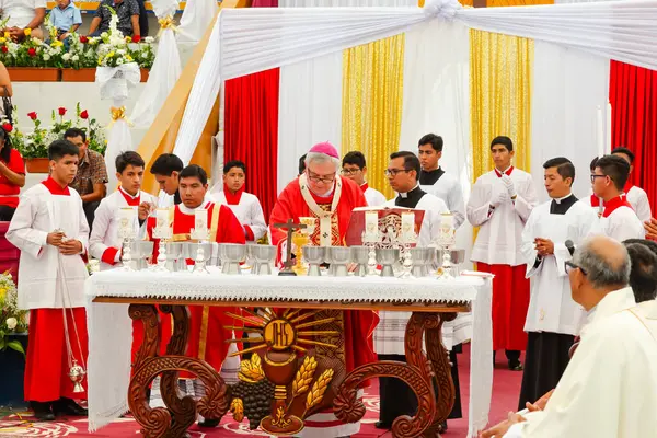 Tumbes, Tumbes, Peru 21-10-2023, Onay Töreni: Bir grup kırmızı ve beyaz üniformalı adam bir rahiple birlikte masanın etrafında toplandı. Rahip elinde bir mum tutuyor ve dini bir törene önderlik ediyor. Adamlar giyinmiş..