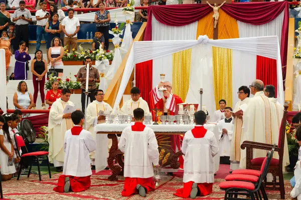 Tumbes, Tumbes, Peru 21-10-2023, Onaylama Ayini: Bir grup rahip beyaz cüppeli bir adamın elinde bardak ile masanın önünde diz çöküyor. Sahne dini bir tören ya da toplantı gibi görünüyor.
