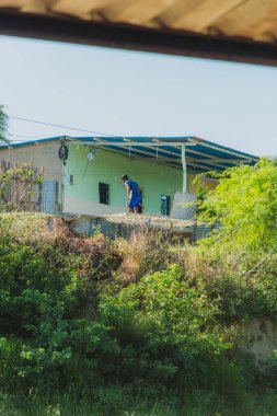 Bir adam bir evin çatısında duruyor. Ev yeşil ve mavi bir çatısı var.