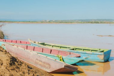 Suda üç tekne var ve biri yeşil renkte. Su kahverengi ve gökyüzü mavi.