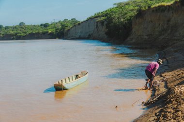 Arka planda teknesi olan bir adam nehirde balık tutuyor. Su kahverengi ve bulanık.