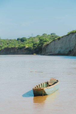 Yeşil renkli bir nehirde küçük bir tekne yüzüyor. Su kahverengi ve gökyüzü mavi.