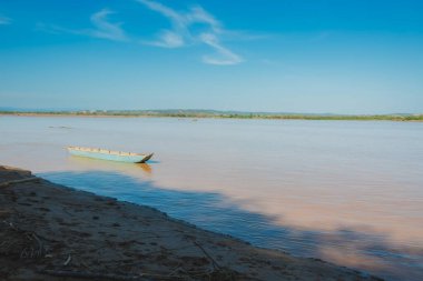 Arka planda mavi gökyüzü olan bir tekne nehirde yüzüyor. Su açık pembe bir renktir.