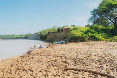 Üzerinde nehir ve tekne olan bir sahil. Kumsal kumlu ve su sakin.