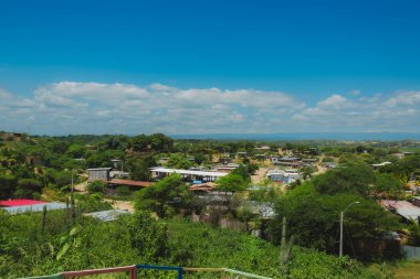 Evleri ve ağaçları olan küçük bir kasaba manzarası. Gökyüzü mavi ve bazı bulutlar var.