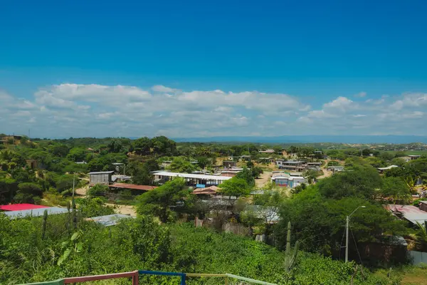 Evleri ve ağaçları olan küçük bir kasaba manzarası. Gökyüzü mavi ve bazı bulutlar var.