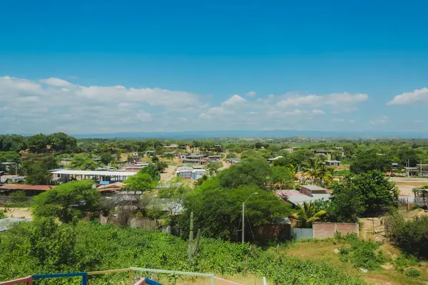 Evleri ve ağaçları olan küçük bir kasaba manzarası. Gökyüzü mavi ve bazı bulutlar var.