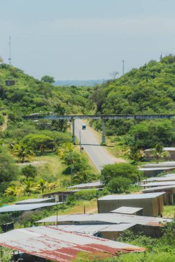 Üzerinde köprü olan bir yol ve arka planda birkaç ev. Yol boş ve gökyüzü temiz.