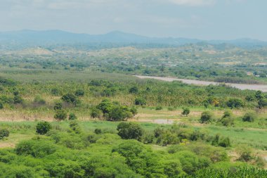 İçinden nehir akan yemyeşil bir tarla. Gökyüzü bulutlu, ama güneş hala parlıyor. Huzurlu ve huzurlu bir sahne.
