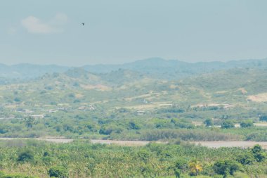 İçinden bir nehrin aktığı güzel bir manzara. Gökyüzü bulutlu ve arka plandaki dağlar ağaçlarla kaplı.