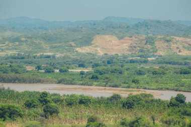 İçinden nehir akan yemyeşil bir vadi. Nehir kahverengi ve çamurlu, ağaçlar uzun ve yeşildir. Huzurlu ve huzurlu bir sahne.