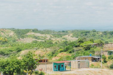 Kırsal alanda küçük bir ev ve birkaç ev daha var. Evler ağaçlarla çevrili ve gökyüzü bulutlu.