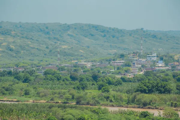 İçinden nehir akan yemyeşil bir vadi. Vadi dağlarla çevrilidir ve uzaklardan evler görülebilir.