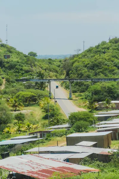 Üzerinde köprü olan bir yol ve arka planda birkaç ev. Yol boş ve gökyüzü temiz.
