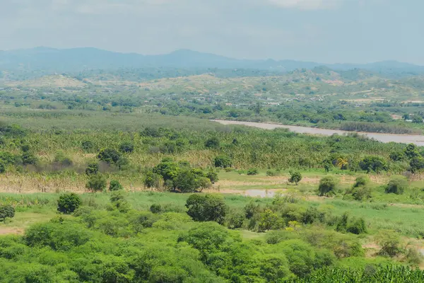 İçinden nehir akan yemyeşil bir tarla. Gökyüzü bulutlu, ama güneş hala parlıyor. Huzurlu ve huzurlu bir sahne.