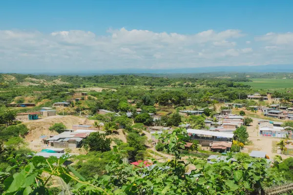 Birkaç evi ve bir sürü ağacı olan bir kırsal bölge. Gökyüzü mavi ve bazı bulutlar var.