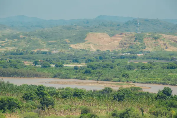 İçinden nehir akan yemyeşil bir vadi. Nehir kahverengi ve çamurlu, ağaçlar uzun ve yeşildir. Huzurlu ve huzurlu bir sahne.