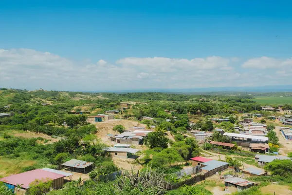 Birkaç evi ve birkaç ağacı olan bir kırsal bölge. Gökyüzü mavi ve bazı bulutlar var.
